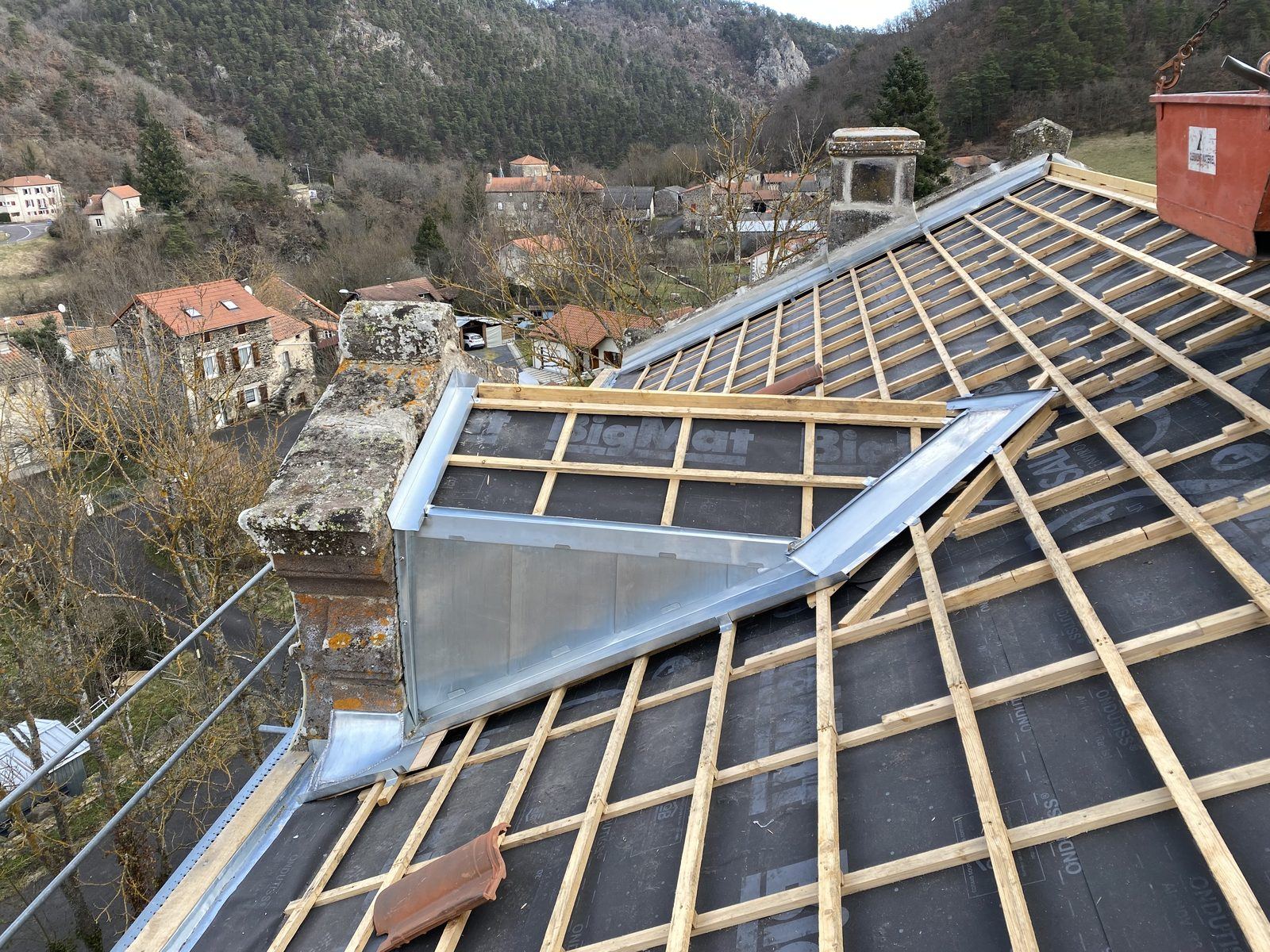 Liteaux et écran sous-toiture, zinguerie autour d’une lucarne, vue sur le village