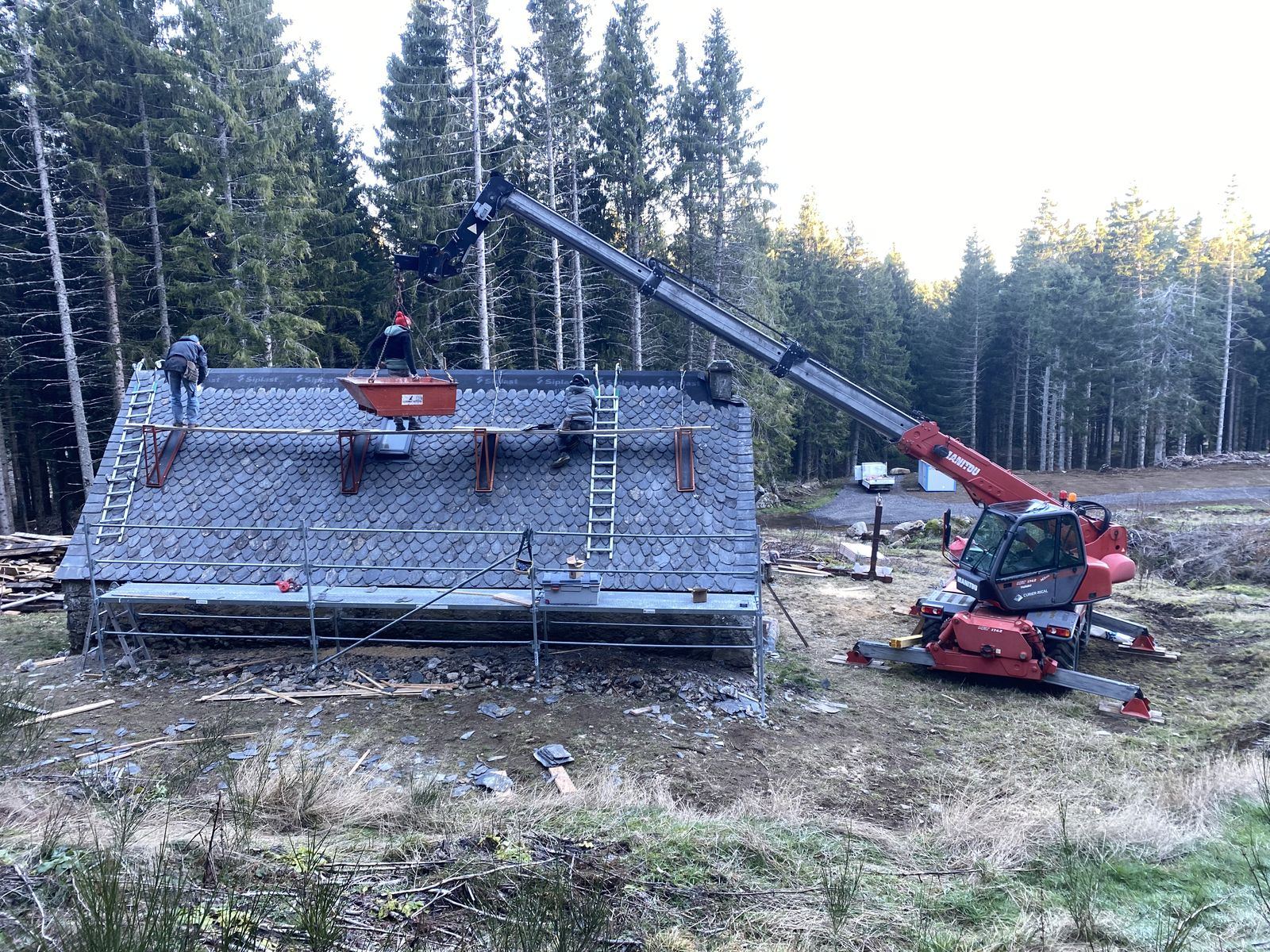 Toiture en ardoise en cours de pose au milieu des sapins, chariot télescopique