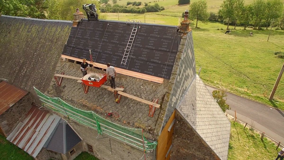 Vue aérienne d’un chantier de couverture : deux couvreurs sur un toit en cours de réfection, entre pierre et écran sous-toiture